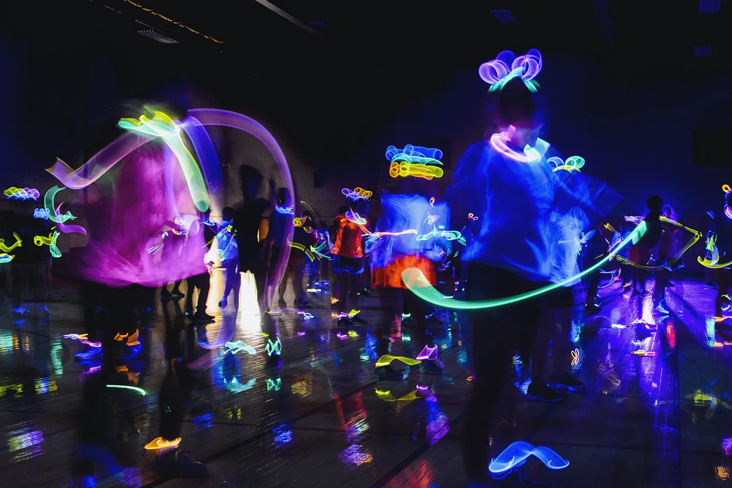 Slow exposure photo showing a crowd of people in a dark room making patterns with glow sticks
